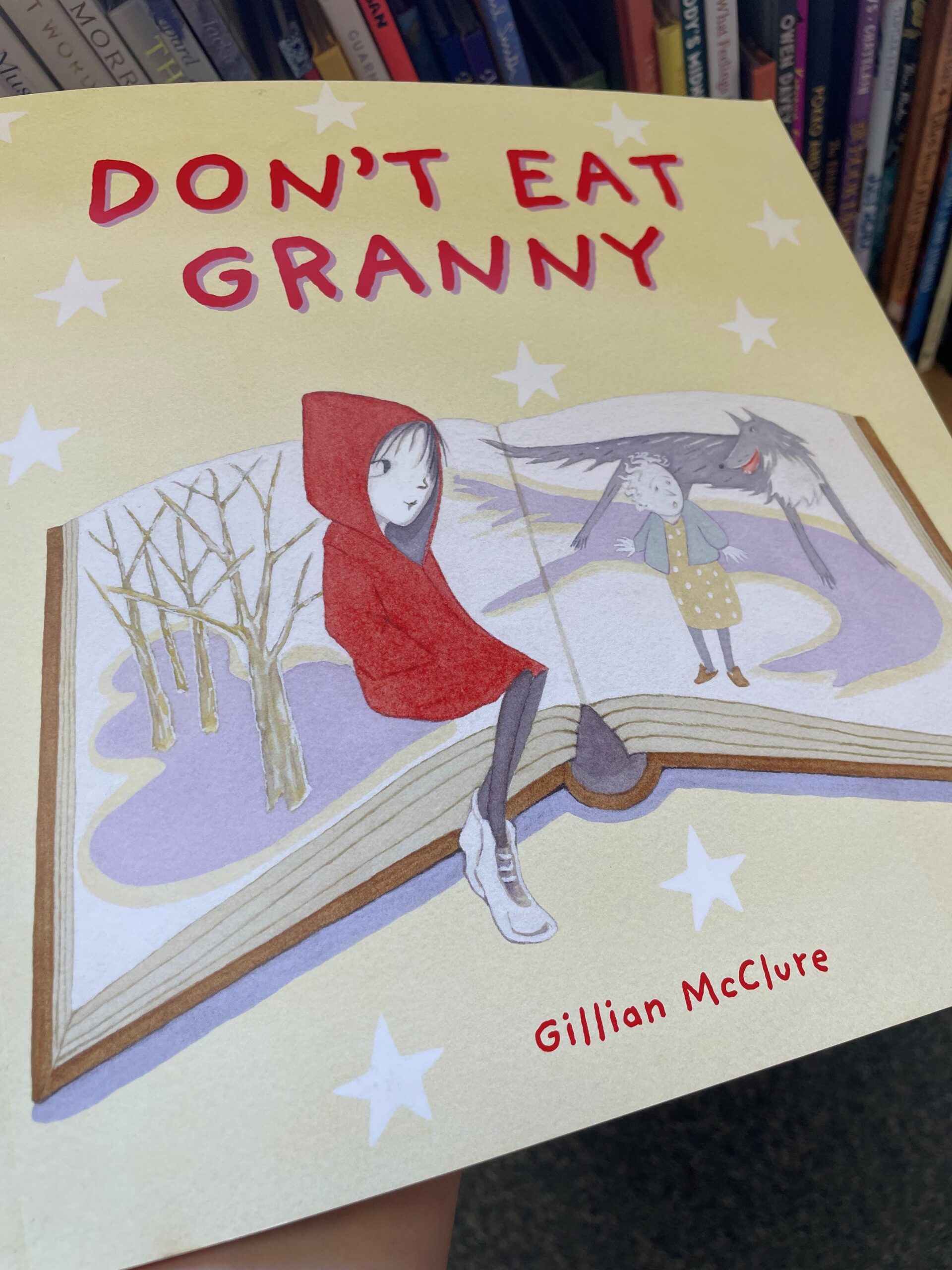 Children's book Don't Eat Granny being held by one hand in front of a bookshelf